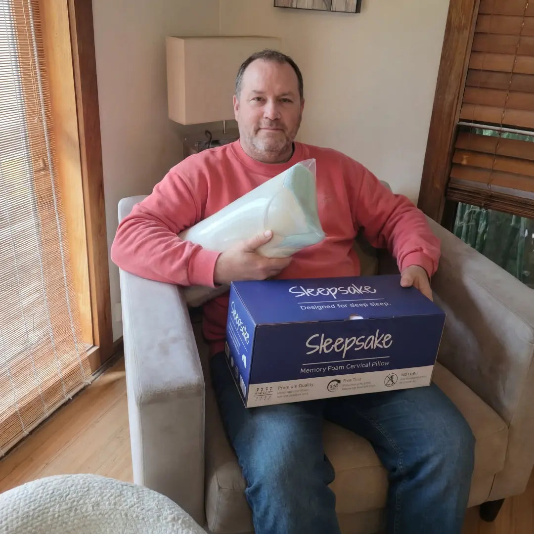 Man sitting on a chair holding a Sleepsake pillow and packaging